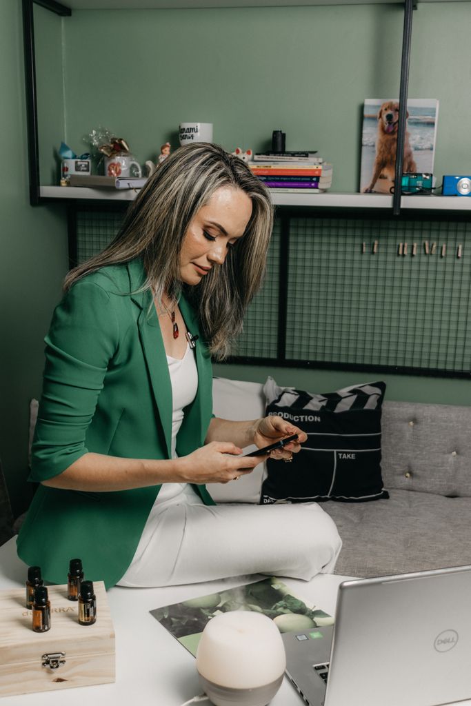 Elegant businesswoman using a smartphone at a desk with essential oils and a laptop, showcasing modern technology.