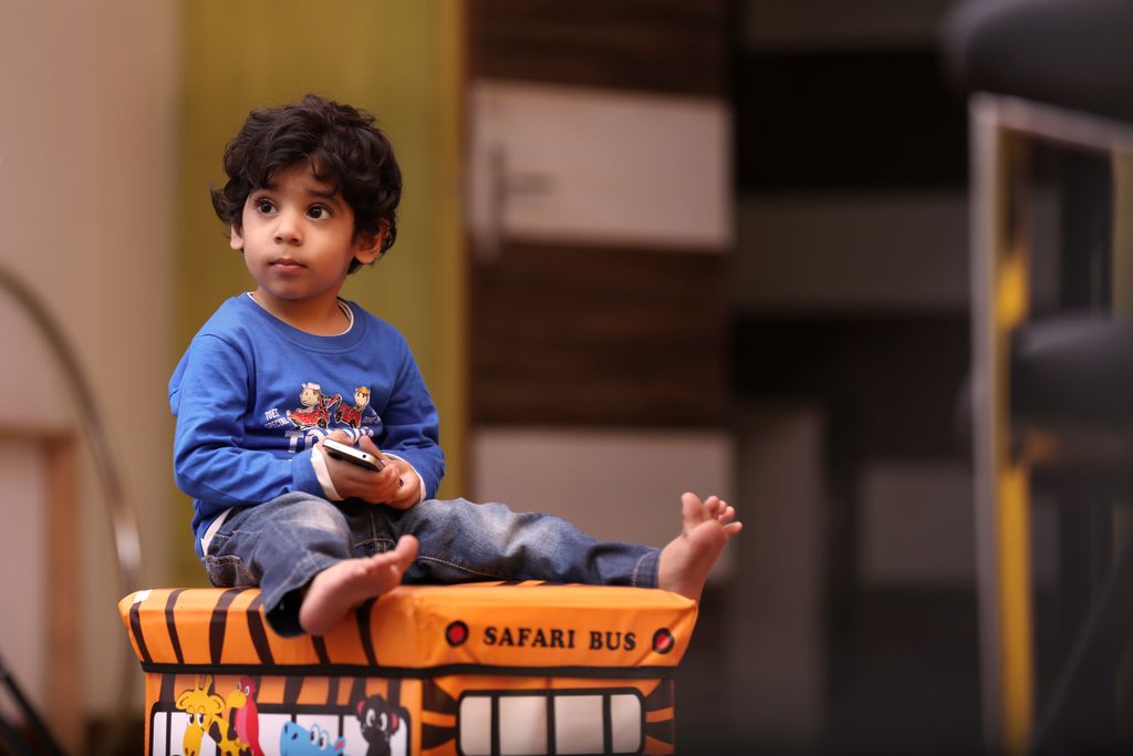 Child sitting on a colorful safari bus toy box indoors.